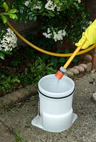 Adding water to weedkiller in garden sprayer, wearing protective rubber gloves for safety