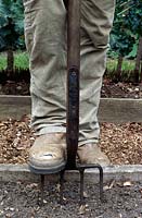 Gardener with worn boots digging a raised vegetable bed