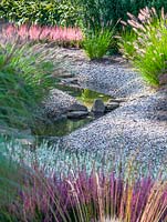Stream winding through gravel garden with Pennisetum alopecuroides and Calluna vulgaris