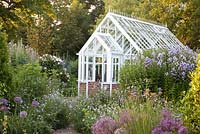 Greenhouse in country cottage garden with planting of Allium christophii, Campanula lactiflora 'Loddon Anne' and Scabiosa arvensis