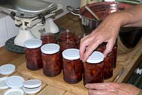 Making Strawberry jam - applying screw tops to full jars to achieve an airtight seal as jam cools
