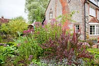 Colourful late summer bed of Berberis, Sage, Eupatorium with Gypsy hut and flint cottage beyond