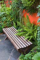 Small town garden with wooden bench, ferns and slate tiled floor. 
