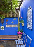 Courtyard with painted blue walls using powder pigment. Wooden benches and decorative tiles under pergola 
