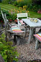 Chairs and square table made of drift wood on graveled corner of cottage garden 