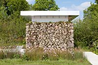 Structure with drystone wall, wooden and metal roof in wet grassland, damp area - Willow grove with Juncus effusesin in border