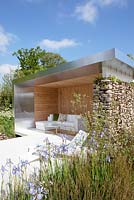 Lounge area in summer shelter - structure built with stone, wood and metal. Blue Iris in border