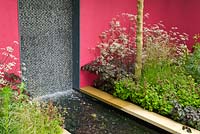 Water cascades down a wall and in to a channel in The Brewin Dolphin Garden at the RHS Chelsea Flower Show. Planting includes: Anthriscus sylvestris 'Ravenswing', Deschampsia cespitosa 'Pixie Fountain' and Geum rivale