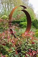 Corten steel sculpture in 'Windows through Time' at the RHS Chelsea Flower Show. Planting includes: Leucothoe 'Zeblid', Cercis canadensis 'Forest Pansy', Cirsium rivulare 'Atropurpureum', Phormium and Roses