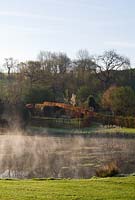 Plaz Metaxu garden at Coombe House, Devon. Mist rising off the lake in front of the Beech Enclosure.