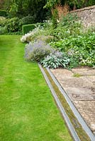A simple rill runs alongside the herbaceous border, including glaucous hostas and geraniums. Upton Wold, Moreton-in-Marsh, Gloucestershire, UK