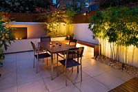 Minimalist Garden lit up at night - Acer Aconitfolium, table and chairs and Phyllostachys Aurea and water feature 