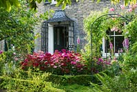 View of formal town garden with Buxus - Box edging, Roses growing on arches over paths. Dianthus - Sweet williams and Digitalis - Foxgloves