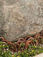 Large boulder with rusty horse shoes and planting of Viola 
