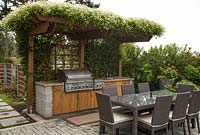 Clematis terniflora growing over pergola sheltering outdoor kitchen