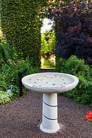 Birdbath inscribed with Twitter names of Anne Wareham and Charles Hawes in their Front Garden. View to tunnel of Carpinus betulus (Hornbeam). Cotinus coggygria 'Grace'. Veddw House Garden, Monmouthshire, Wales