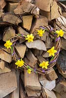 Woven daffodil wreath against stack of logs. Narcissus 'Tete a tete'