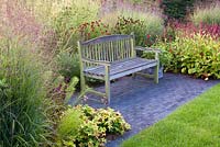 Wooden garden bench. Beds of prairie planting.  Panicum virgatum 'Shenandoah', Helenium 'Rubinkuppel', Persicaria amplexicaulis 'Taurus', Veronicastrum virginicum 'Fascination'. 