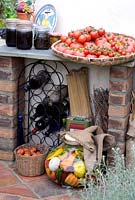 Mediterranean oven in garden setting for alfresco cooking, with tray of tomatoes and jars of pickles and preserved vegetables