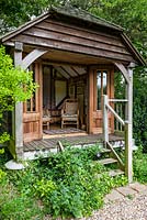 Wooden summerhouse, raised on stilts. Through the steps grow clematis and ivy - Hedera helix with green alkanet - Pentaglottis sempervirens next to them.  The roof was shingled by hand.