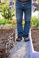 Man constructing gravel path in vegetable garden. Adding gravel and firming. 