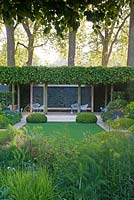 The Telegraph Garden, RHS Chelsea Flower Show 2014, gold medal winner. View from under pleaching, with sunburst, across Italianate garden to stone wall panel in boundary hedge and loggia at rear. Buxus sempervirens, Tilia x Europea 'Pallida' pleaching 