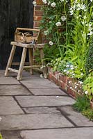 View along path to stool with garden implements, accompanied with border planting of Rosa 'Adelaide d'Orleans', Camassia leichtlinii 'Alba', Dryopteris filix-mas and Nepeta x faassenii 'Alba'. The Topiarist's Garden. 