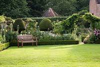 Clipped topiary and garden seat overlooking formal lawn with summer planting of Rosa, Papaver, Leucanthemum, Digitalis, Euphorbia, Fennel. Chenies Manor, Buckinghamshire