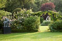 The Dreamer sculpture by Carol Donaldson alongside mixed Rosa and archway in summer. Chenies Manor, Buckinghamshire