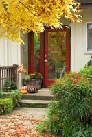 Fall entry garden with red door, pathway, containers with fall decor. Nandina domestica - Heavenly Bamboo, Acer palmatum - Japanese Maple.