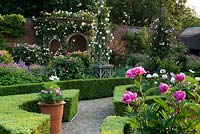 Walled garden with ornate wooden obelisks and arbour. Very floral scene with pink peonies.  Seend, Wiltshire