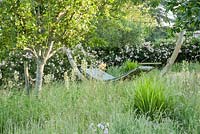 Hammock in the orchard surrounded by long grass, white camassias and meadow cranesbill. Forest Lodge, Pen Selwood, Somerset, UK