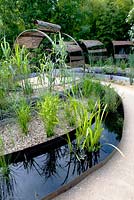Title: Le Jardin Dechene. Pergolas made of a construction of metal hoops. Borders in plateaus planted with  Arundo donax and in the oval shaped pools aquatic plants like Menyanthes trifoliata,