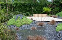 Title: Pour L Amour de Tongariro. Garden with wooden path passing several 'volcanos' planted with sedums and covered with broken black slates.
