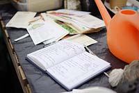Notebook, Seed packets and watering can on a workbench, Wales, UK.