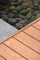 Detail of wooden walkway/platform above shallow pool, with medium sized pebbles in its base - London City Garden - RHS Hampton Court Flower Show 2014 
 