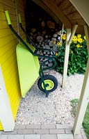Bright yellow shed with roundshaped windows. Green baroow under shelter.