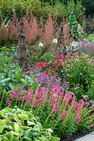 Long deep perennial border with a variety of perennials at successive heights with two woven obelisks. August, Surrey