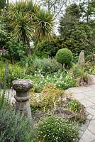 A courtyard garden largely planted with for foliage features clipped box, grasses, euphorbias, corokia, cordylines and bamboos around standing stones, architectural fragments and old galvanised tubs used as ponds, planters or mini water gardens.