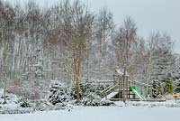Country garden in winter with childrens play area and deciduous forest behind 
