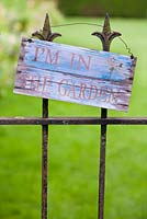 Wooden sign on wrought iron gate, reading 'I'm in the garden'.