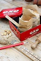 Saved garden seed in paper packets in OXO tin, with wooden dibber, ruler and garden items