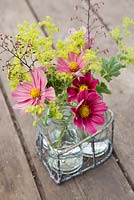 Floral display of cosmos, alchemilla mollis and heuchera flowers in small glass jars