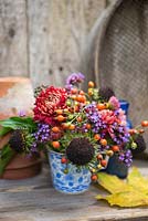 Floral display of rose hips, helianthus seed heads, verbena and chrysanthemum in blue and white tea cup. 