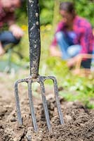 Fork embedded in soil, man and woman working in background