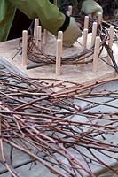 Using a peg frame to form the circular base of a wreath out of long twigs .