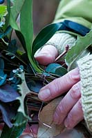 Attaching a spring of foliage to the twig frame of the wreath.