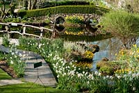 Garden view in springtime with daffodils, little lake, bridge 