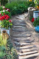 Mediterranean style garden, path made from drift wood, log pathway leading through garden, pelargoniums and lemon tree planted in olive oil tins