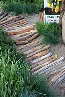 Mediterranean style garden, path made from drift wood, log pathway leading through garden,  planted with grass, herbs, with lemon tree planted in olive oil tin 